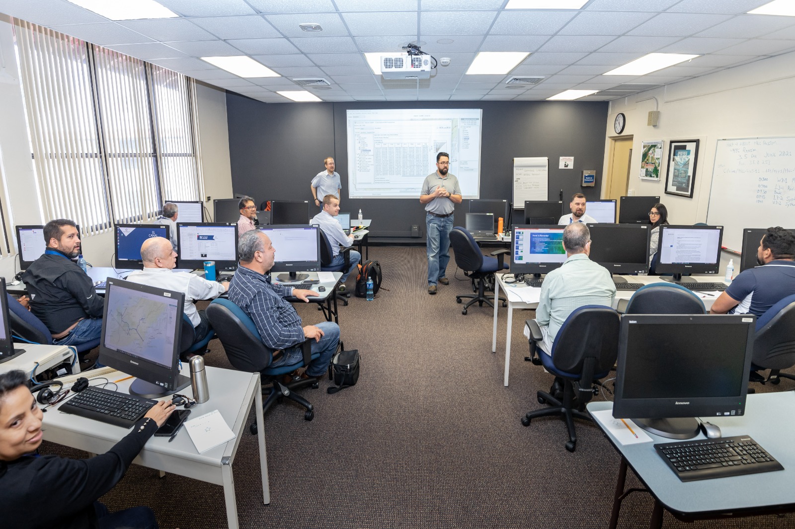 evan heisman and david bogema standing before the class lecturing, viewed up the center aisle of the computer lab