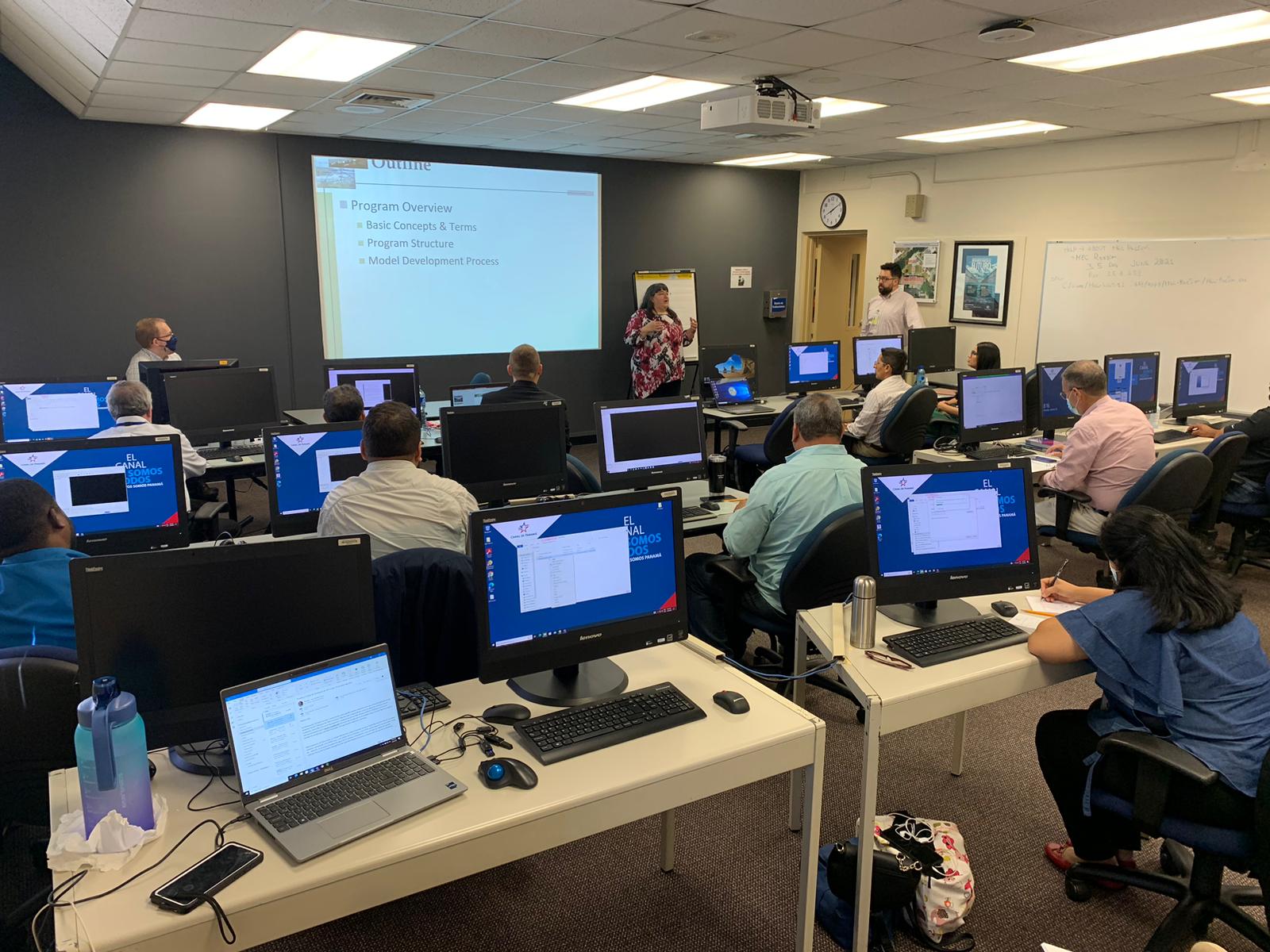 joan klipsch stands in front of a projector screen teaching to students seated in a computer lab