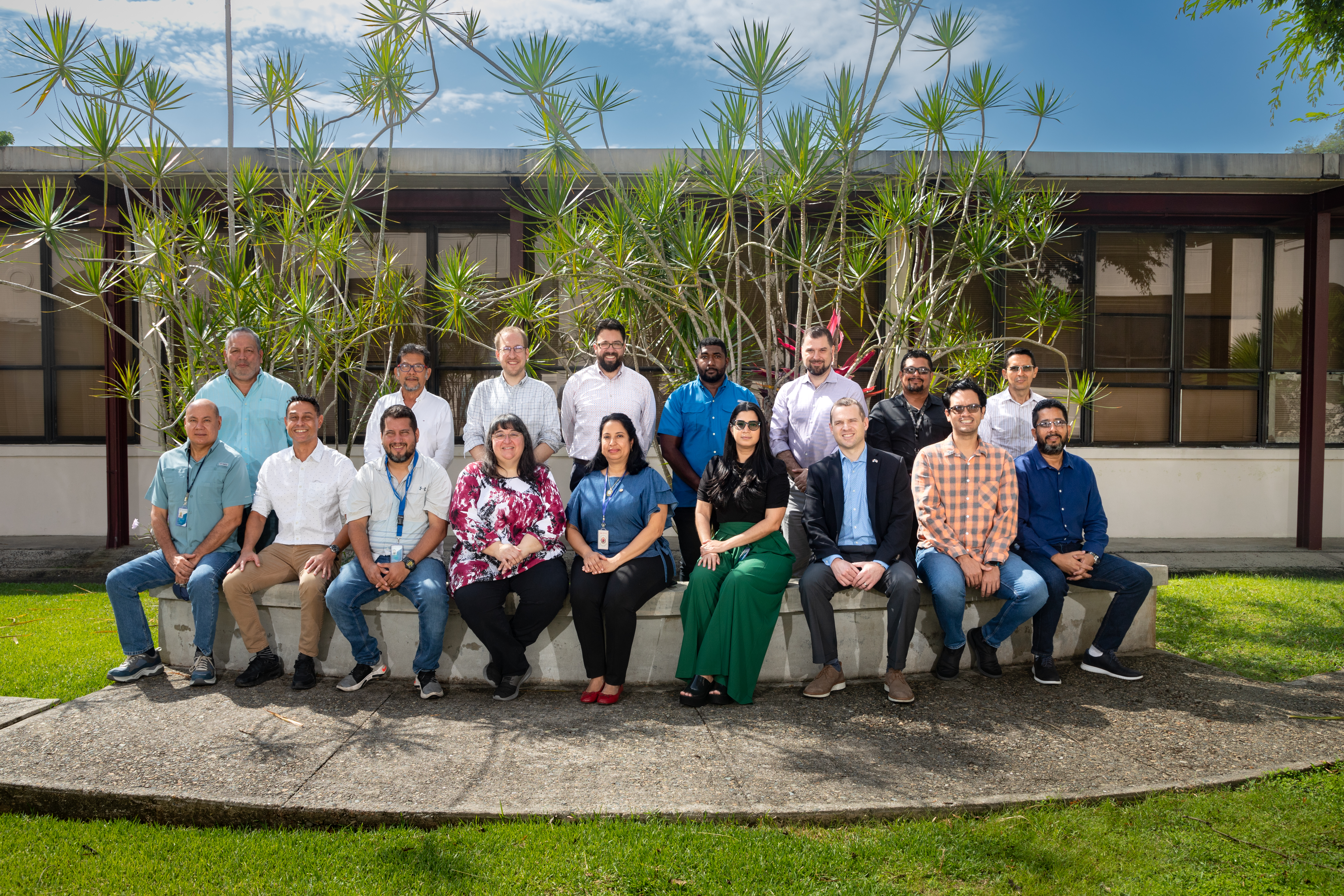 class photo of students and instructors seated and standing around a bench with a cloudy blue sky behind