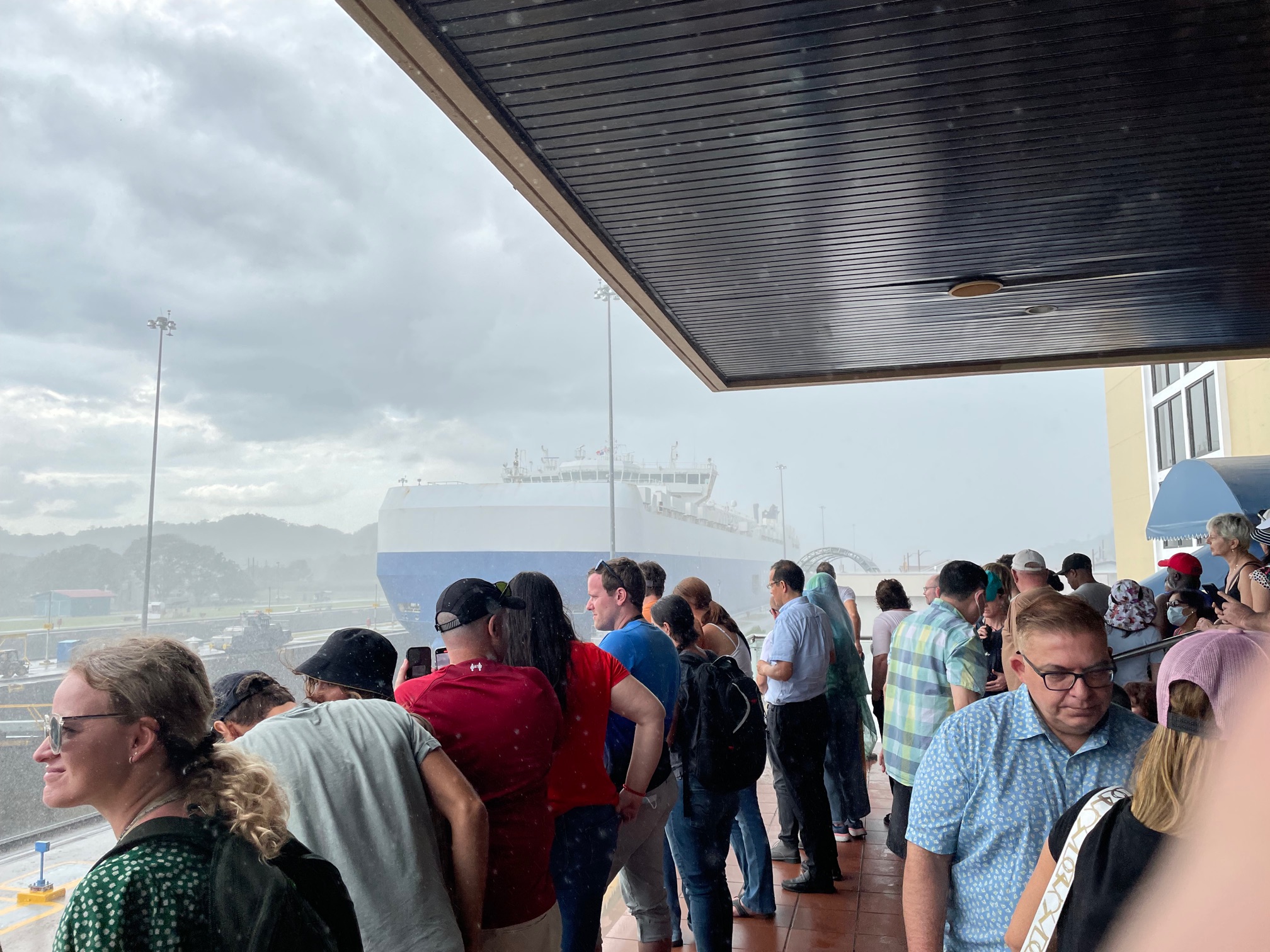 crowd gathered to watch a blue and white vehicle carrier passing through the panama canal at the miraflores locks visitor center